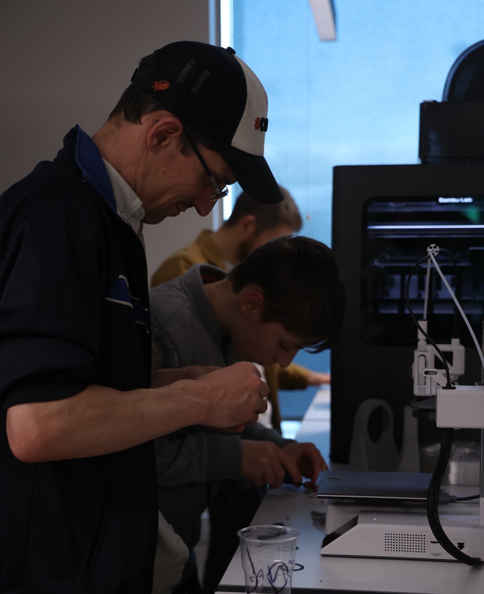 Builders soldering at a bench next to a 3D printer